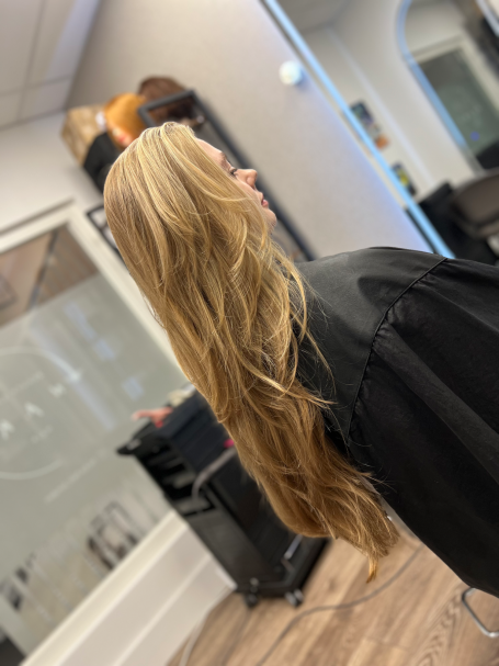 Woman with long, wavy blonde hair facing sideways in a salon setting.